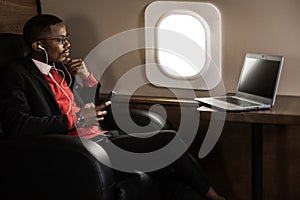 Successful young Afro American black businessman sitting in the chair of his private jet