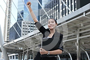 Successful young Asian business woman raising hands with modern buildings city background.