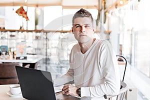 Successful young business man in a white shirt with a modern computer sits in a cafe. Cool freelancer guy working remotely