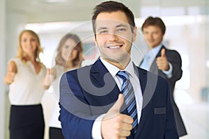 Successful young business people showing thumbs up sign while standing in office interier