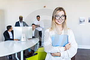 Successful young business woman in glasses standing in front of multi ethnic group of people in office