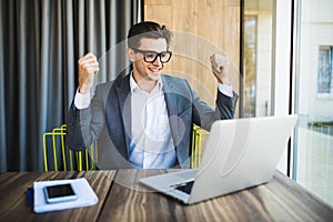 Successful young businessman enjoying success at his desk. Victory