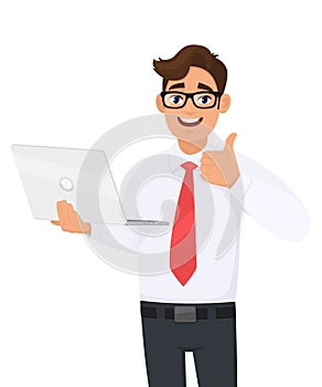 Successful young businessman holding laptop computer and making thumbs up gesture. Person showing  good, agree or approval sign.