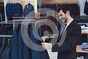 Successful young businessman looks at jacket in business mens clothing store.