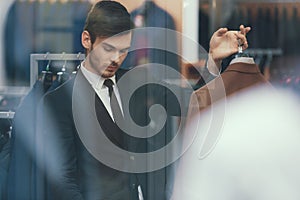 Successful young businessman looks at jacket in business mens clothing store.