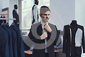 Successful young businessman measures jacket in business mens clothing store.