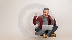 Successful young businessman screaming and pumping fists while reading e-mails over laptop. Male professional celebrating his