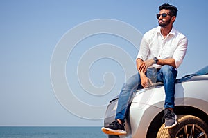 Successful young businessman sunglasses on a beach. Afro man leaning on his car parked in front of ocean on road trip