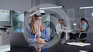 Successful young businesswoman in virtual reality headset working in modern office