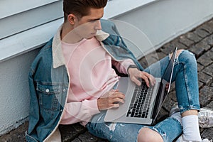 Successful young freelancer man in stylish denim casual jeans clothes sits with laptop and works remotely on creative project.