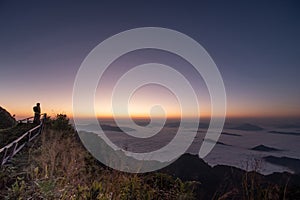 Successful young man backpacker on top of a mountain.Hiker standing on mountain peak waiting for sunrise