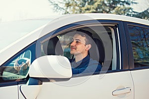 Successful young man driving his new white car keeps hand on the steering wheel looking ahead happy feeling safe. Confident