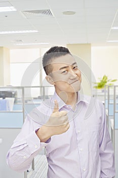 Successful young man giving thumbs up sign in office, portrait