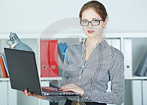 Successful young woman holding laptop in hands looking in camera.