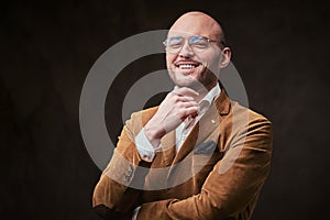 Successfull bald businessman posing in a studio wearing stylish velvet jacket, white shirt and glasses