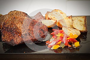 Succulent thick juicy portions of grilled fillet steak served with roasted potatoes and peppers on black granite board