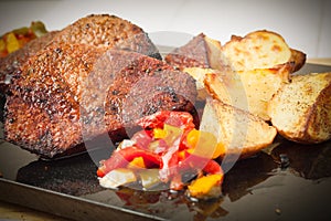 Succulent thick juicy portions of grilled fillet steak served with roasted potatoes and peppers on black granite board