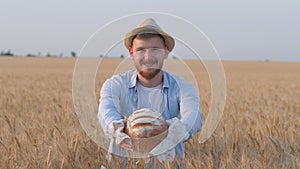Sucessful young farmer, happy rural guy gives you tasty rooty and smiles staying in grain wheat bread field at autumn