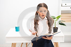 Such difficult topic. Studying difficulties. Girl read book while stand table white interior. Schoolgirl studying