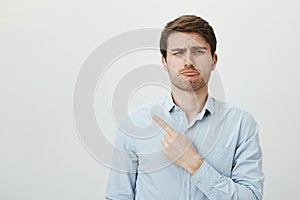 Such shame I missed all fun. Portrait of handsome sad caucasian guy pointing left with index finger whining and looking