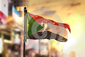 Sudan Flag Against City Blurred Background At Sunrise Backlight