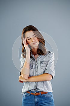 Suffering with a headache. Studio shot of an attractive young woman suffering with a headache against a grey background.