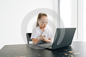 Suffering from pain little girl with broken hand wrapped in white plaster bandage touching injured arm sitting at table