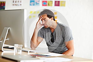Suffering from writers block. A handsome man sitting at a desk and looking at a computer screen with head rested on his