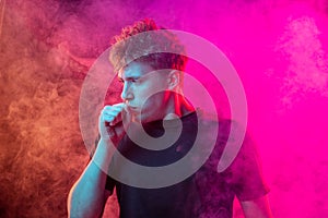 Suffocate in the smoke. Scared young man with stressed emotions isolated over pink background with clouds of smoke