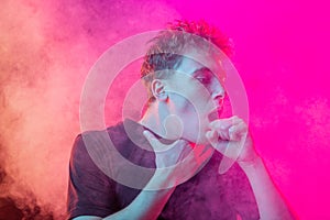Suffocate in the smoke. Scared young man with stressed emotions isolated over pink background with clouds of smoke