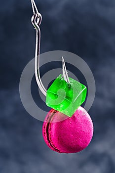 Sugar addiction by food producers concept. Macaroon and candy on a fishing hook