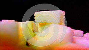 Sugar being pored onto a pile of sugar cubes. Against black background