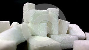 Sugar being pored onto a pile of sugar cubes. Against black background