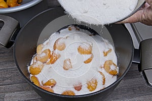 Sugar being poured over the layers of fruit and sugar in the saucepan