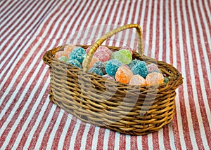 Sugar coated jelly sweets in wicker basket on striped tablecloth