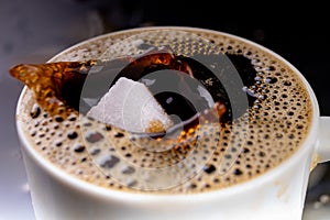 A sugar cube dropped into a cup with black coffee. Falling sugar into a warm drink