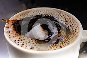 A sugar cube dropped into a cup with black coffee. Falling sugar into a warm drink