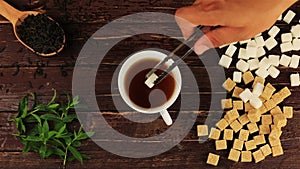 Sugar cubes added into tea glass on him located brown and white sugar cubes, spoon with tea leaves, mint leaves on brown