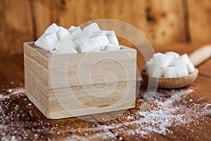 Sugar Cubes in Square Shaped Bowl with Unrefined Sugar spill over in Wooden Background. photo