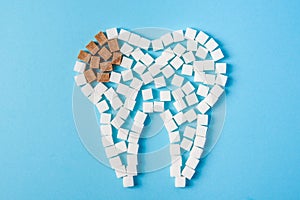 Sugar destroys the tooth enamel and leads to tooth decay. Tooth made of white and caries made of brown sugar cubes.