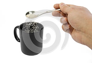 Sugar falling from spoon in man hand into a cup