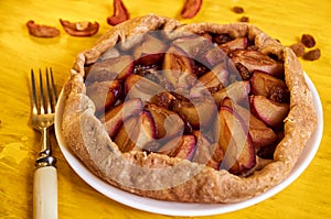 Sugar free pie with plums and raisins on a white plate on yellow wooden background decorated with fresh plums, brown raisins