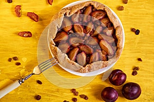 Sugar free pie with plums and raisins on a white plate on yellow wooden background decorated with three fresh plums