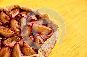 Sugar free pie with plums and raisins on yellow wooden background close up with copy space on the right side