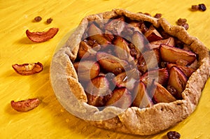 Sugar free pie with plums and raisins on yellow wooden background close up decorated with brown raisins and dried pieces of apple