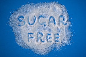 Sugar Free words hand written on a heap of white sugar on a blue background top view. Stop diabetes and excessive sugar intake con