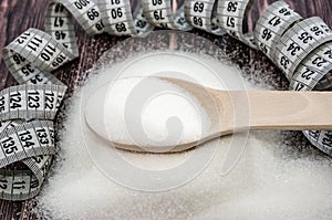Sugar and measuring tape on a wooden background. The concept of weight loss, diet.