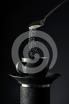 Sugar is poured into a black cup of coffee on a black background