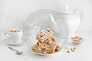 Sugar powder is pouring on Viennese wafers with walnuts and splashing coffee on breakfast table.