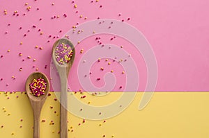 Sugar sprinkle dots In a wooden spoon on pink and yellow background,decoration for cake and bakery